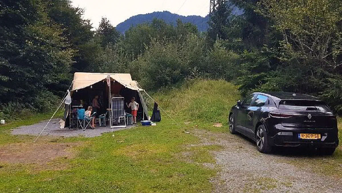 Tent en deelauto op een natuurcamping, die rijk is aan bomen.
